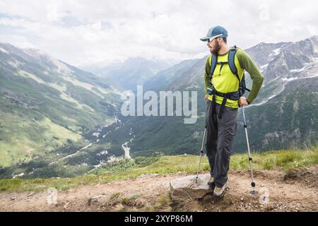 Portrait d'un jeune voyageur avec une barbe et un sac à dos dans une casquette et des lunettes de soleil sur fond des montagnes du Caucase. Journée ensoleillée. Le conc Banque D'Images