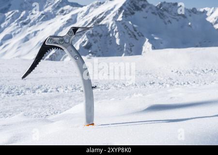 Gros plan d'une hache glacée dans la neige avec des montagnes enneigées en arrière-plan Banque D'Images