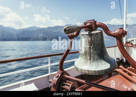 Proue d'un bateau avec cloche de bateau lors d'une croisière. Eau bleue, chaîne de montagnes et mignon petit village à Lago di Garda, Italie, Europe Banque D'Images