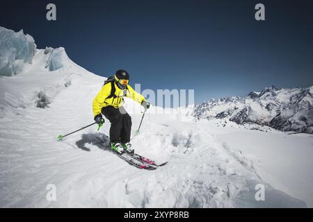 Skieur professionnel à la vitesse avant de sauter du glacier en hiver contre le ciel bleu et les montagnes Banque D'Images