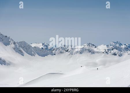 L'alpiniste se tient au bord du glacier avec une pelle à neige dans ses mains et montre le geste de Shak contre le ciel bleu et le mont du Caucase Banque D'Images