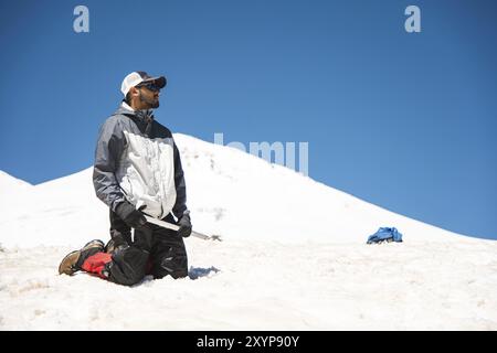 Entraînement pour corriger le glissement sur une pente ou un glacier à l'aide d'une hache de glace. Un routard entièrement équipé s'agenouille sur une pente enneigée dans les montagnes à proximité Banque D'Images