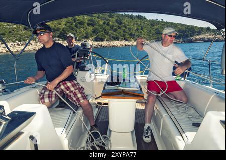 3 hommes d'un équipage de voile à l'arrière de leur yacht lors d'une manœuvre de voile Banque D'Images