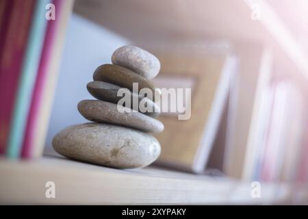 Feng Shui : cairn en pierre à la maison dans une étagère à livres, livres flous au premier plan et en arrière-plan. Équilibre et relaxation. Lumière du soleil Banque D'Images