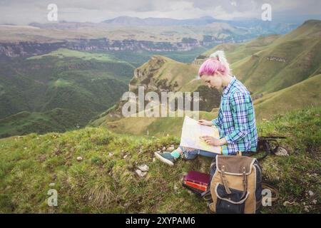 Voyageuse fille avec des cheveux multicolores assis sur la carte de lecture de la nature et tenant une boussole à la main. Le concept de navigation dans la recherche et le tourisme i Banque D'Images