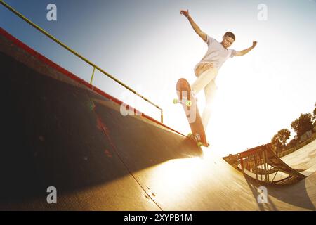 Adolescent patineur raccroché au-dessus d'une rampe sur une planche à roulettes dans un skate Park. Grand angle Banque D'Images