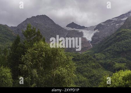 Paysage vertical, une lumière du soleil à travers les nuages illumine sélectivement une partie de la pente au pied des roches caucasiennes de la haute Balkarie Banque D'Images