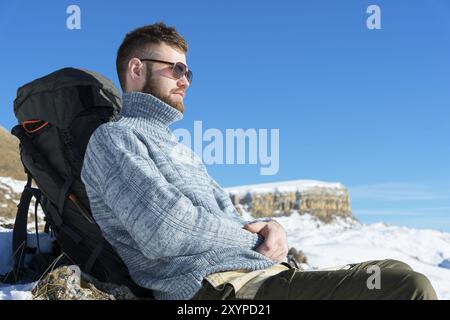 Portrait d'un voyageur Hipster en lunettes de soleil et un pull gris tricoté reposant sur la toile de fond d'un beau paysage hivernal avec une table Mo Banque D'Images