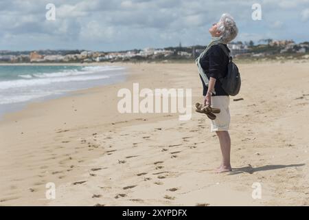 Une personne âgée se tient sur la plage et tient son visage au soleil Banque D'Images