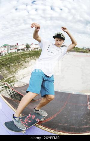 Adolescent patineur raccroché au-dessus d'une rampe sur une planche à roulettes dans un skate Park. Grand angle Banque D'Images