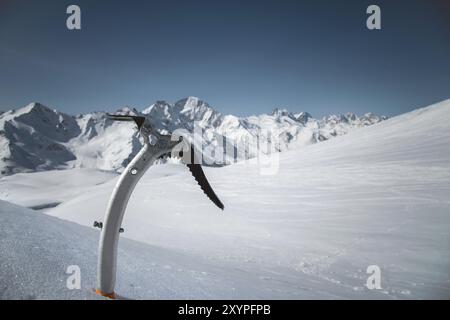 Gros plan d'une hache glacée dans la neige avec des montagnes enneigées en arrière-plan Banque D'Images