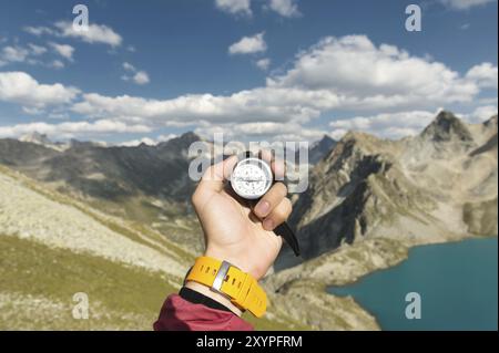 La main d'un homme tient une boussole magnétique de poche pour la navigation sur la toile de fond d'une pente rocheuse et d'un lac de montagne. Le concept de trouver un moyen. G Banque D'Images