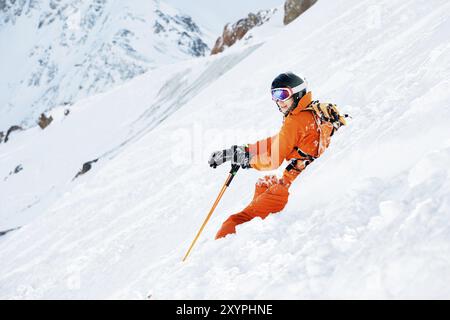 Un skieur dans une combinaison orange et avec un sac à dos est assis heureux dans la neige après être tombé. Le concept de loisirs dans les montagnes et le ski Banque D'Images