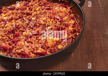 Un grand poêle en fonte avec chili con carne, plat traditionnel Mexicain, sur un fond sombre avec copie espace Banque D'Images