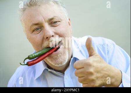 Senior avec piment rouge et vert dans la bouche lève le pouce Banque D'Images