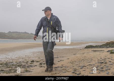 Photographe sur la plage de l'estuaire de la rivière Camel dans la baie de Padstow sous la pluie Banque D'Images