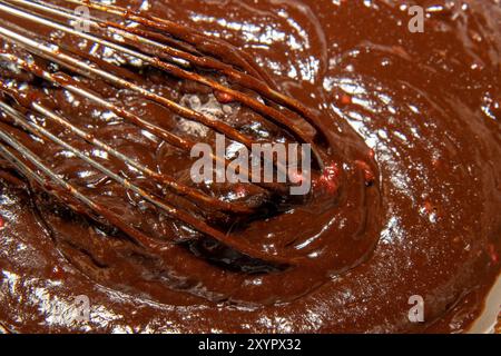 Un fouet de cuisine mélangeant le mélange de chocolat pour faire un trey de framboises dans des brownies au chocolat Banque D'Images