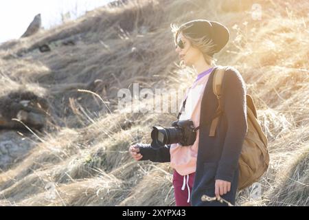 Femme photographe hippster avec appareil photo reflex numérique. Fille élégante en lunettes de soleil avec un appareil photo sur la nature Banque D'Images