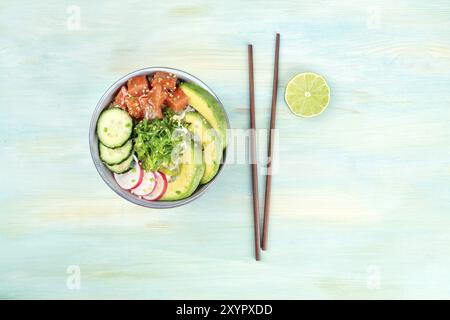 Une photo prise à la verticale de poke, Hawaii traditionnelle salade de poisson cru avec du thon, concombre, avocat, radis, et wakamé, avec des baguettes, une tranche de lime et cop Banque D'Images