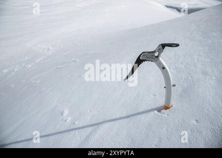 Gros plan d'une hache glacée dans la neige avec des montagnes enneigées en arrière-plan Banque D'Images