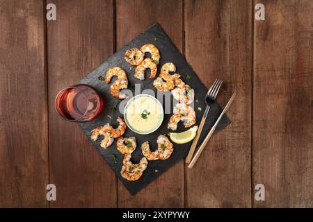 Une photo prise à la verticale du plateau de crevettes cuites sur un fond rustique foncé, avec une sauce et un verre de vin, avec copie espace Banque D'Images