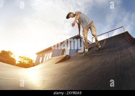 Adolescent patineur raccroché au-dessus d'une rampe sur une planche à roulettes dans un skate Park. Grand angle Banque D'Images