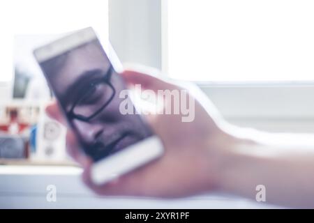 L'homme est titulaire d'un téléphone intelligent à la main, reflet de son visage sur l'écran Banque D'Images