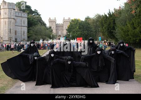 Windsor, Royaume-Uni. 30 août 2024. Extinction Rebellion a organisé une manifestation sur la longue marche avec pour toile de fond le château de Windsor à Windsor, Berkshire ce soir. Les manifestants climatiques de XR portaient des costumes d'affaires et s'habillaient en barons du pétrole, en magnats des médias et en financiers sans visage. Les Oil Slicks, habillés de costumes noirs avec de la peinture de visage noir et blanc, ont réalisé une action théâtrale chorégraphiée dans le but de mettre en évidence le récit XR pour la journée, que le système est brisé. Les rebelles XR campent à Home Park en face du château de Windsor aujourd'hui et pendant le week-end dans le cadre de leur surclassement de trois jours Banque D'Images