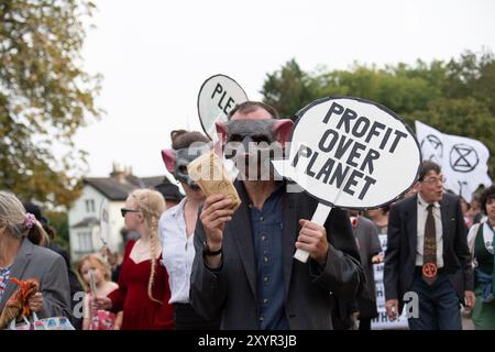 Windsor, Royaume-Uni. 30 août 2024. Extinction Rebellion a organisé une manifestation sur la longue marche avec pour toile de fond le château de Windsor à Windsor, Berkshire ce soir. Les manifestants climatiques de XR portaient des costumes d'affaires et s'habillaient en barons du pétrole, en magnats des médias et en financiers sans visage. Les Oil Slicks, habillés de costumes noirs avec de la peinture de visage noir et blanc, ont réalisé une action théâtrale chorégraphiée dans le but de mettre en évidence le récit XR pour la journée, que le système est brisé. Les rebelles XR campent à Home Park en face du château de Windsor aujourd'hui et pendant le week-end dans le cadre de leur surclassement de trois jours Banque D'Images