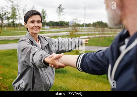 Portrait d'une femme âgée souriante tenant la main de partenaires masculins travaillant régulièrement ensemble au parc de la ville, espace copie Banque D'Images