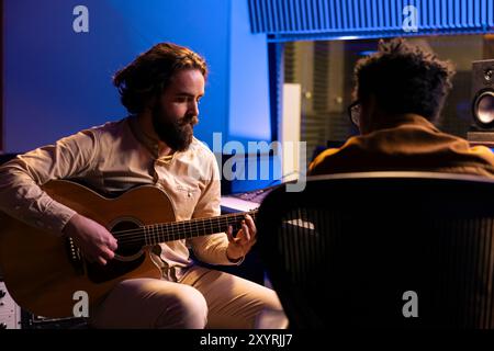 Chanteur jouant de la guitare électro-acoustique pour enregistrer ses airs et composer une chanson à succès, en collaboration avec un technicien audio. Jeune artiste qualifié exécutant de la musique en studio professionnel, post-production. Banque D'Images