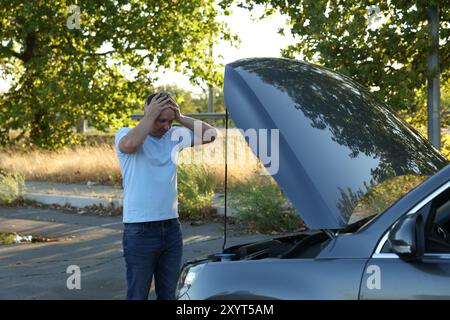 Homme stressé regardant sous le capot de la voiture cassée à l'extérieur Banque D'Images