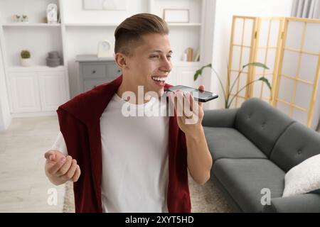 Jeune homme enregistrant un message vocal via smartphone à la maison Banque D'Images