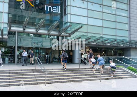 Hong Kong, Chine - 03 juillet 2024 : les gens montent un escalier menant à un grand bâtiment en verre avec un panneau qui dit «centre commercial ifc». Banque D'Images