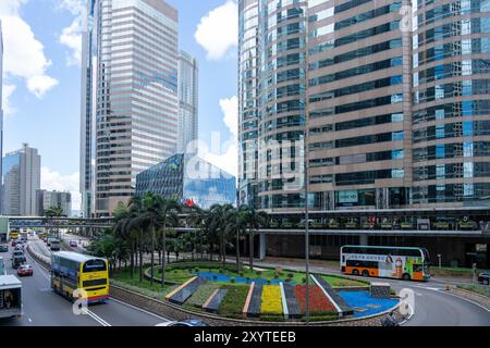 Hong Kong, Chine - 03 juillet 2024 : Une scène de rue à Hong Kong, Chine, avec de hauts gratte-ciel, des bus à impériale, des palmiers, et un rond-point avec f Banque D'Images