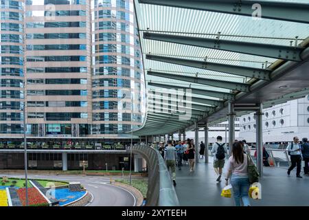 Hong Kong, Chine - 3 juillet 2024 : Un pont piétonnier relie deux gratte-ciel dans le centre de Hong Kong, Chine. Les gens traversent le pont avec l'ic Banque D'Images
