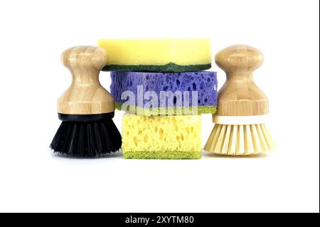 Trois éponges, chacune d'une couleur différente violet, jaune et bleu et deux brosses avec des poignées en bois isolées sur fond blanc, outils de nettoyage Banque D'Images