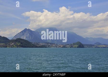 Scène estivale dans les Alpes suisses. Des nuages rampants traversent le sommet du mont Stockhorn. Village Spiez et lac turquoise Thunersee Banque D'Images