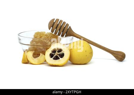 Bol en verre débordant de miel et de plongeoir en bois reposant sur son bord entouré de fruits de coing vibrants, à la fois tranchés et entiers isolés sur fond blanc Banque D'Images