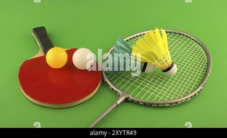 Raquette de tennis de table avec une balle jaune et une balle blanche dessus et raquette de badminton avec un volant de plume sur fond vert clair Banque D'Images