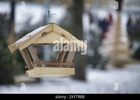 Mangeoire à oiseaux en bois, en forme de petite maison, suspendue à une ficelle dans un environnement enneigé, le fond est flou, contenant des arbres couverts de neige Banque D'Images