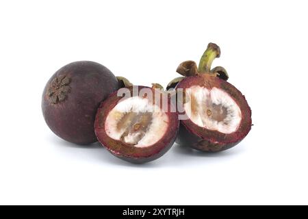 Entiers et coupés en deux fruits de mangoustan révélant sa chair intérieure blanche parsemée de taches violettes foncées et contenant deux graines noires visibles isolat Banque D'Images