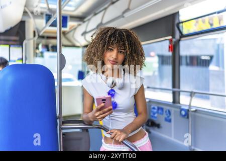 Beauté latine jeune femme avec les cheveux bouclés en utilisant le téléphone debout dans le bus urbain Banque D'Images