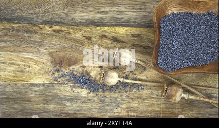 Petit bol en bois rempli de graines de pavot noir et de têtes de graines de pavot séchées sur une table en bois rustique Banque D'Images