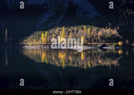 Le Vordere Gosausee en automne. Une partie du chemin autour du lac se trouve dans le soleil, la scène se reflète dans l'eau. Arbres dans les feuilles d'automne. Bien nous Banque D'Images