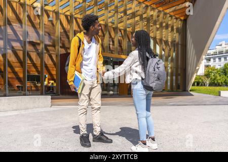 Deux hommes et femmes jeunes amis africains occasionnels se tenant la main et parlant sur le campus universitaire Banque D'Images