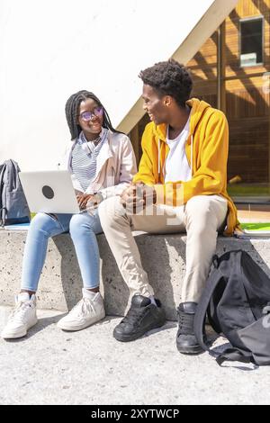 Photo verticale de jeunes amis africains masculins et féminins utilisant un ordinateur portable étudiant en ligne à l'extérieur du campus Banque D'Images