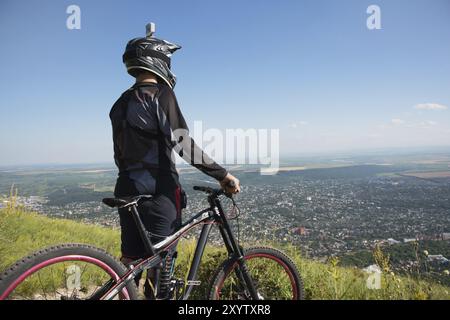 Un jeune gars debout sur votre vélo de montagne au sommet d'une montagne, quand au-dessous des montagnes nuages bas et brouillard Banque D'Images