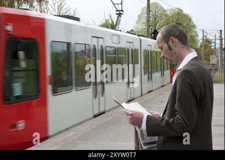 Jeune homme debout sur la plate-forme lisant un journal Banque D'Images