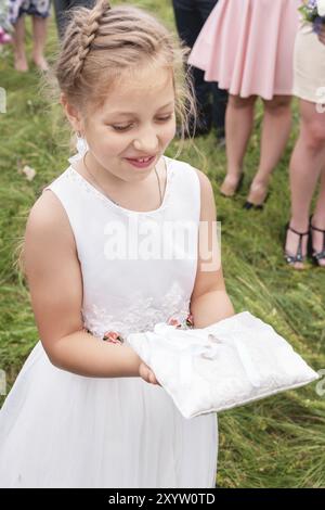 Portrait d'une petite demoiselle d'honneur portant un oreiller avec des anneaux de mariage à la cérémonie de mariage à l'enregistrement de sortie Banque D'Images